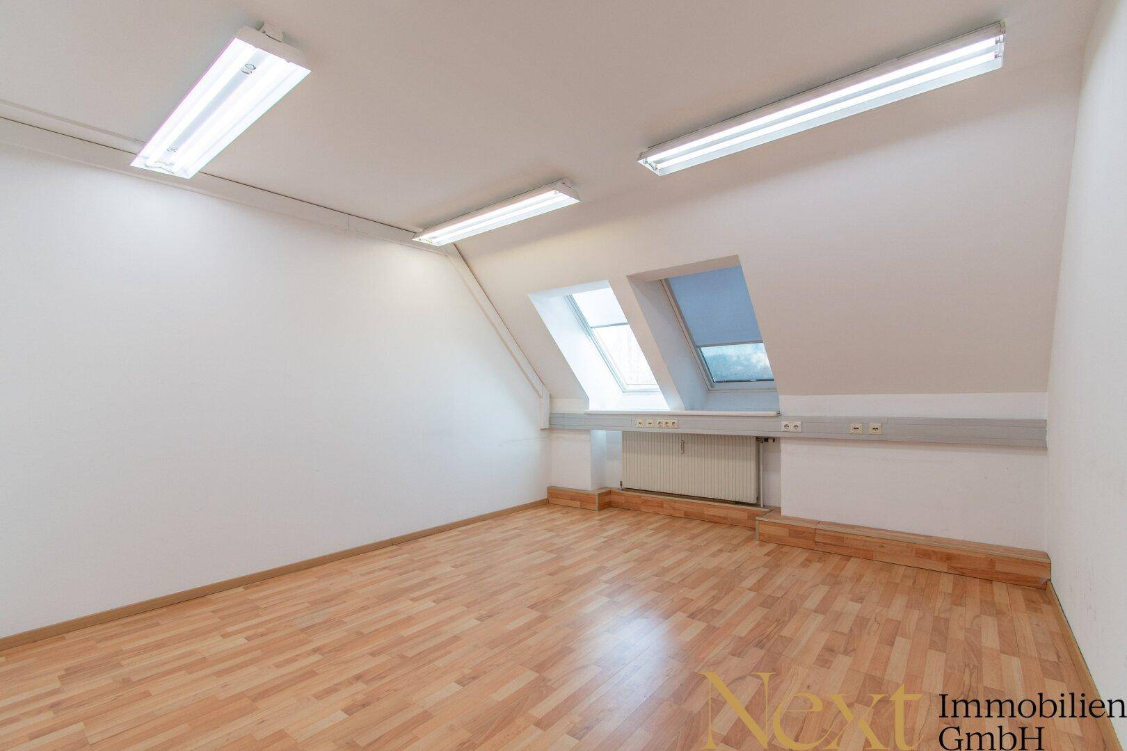Heller Büroraum im Dachgeschoss mit Laminatboden, schrägen Wänden und zwei Dachfenstern.