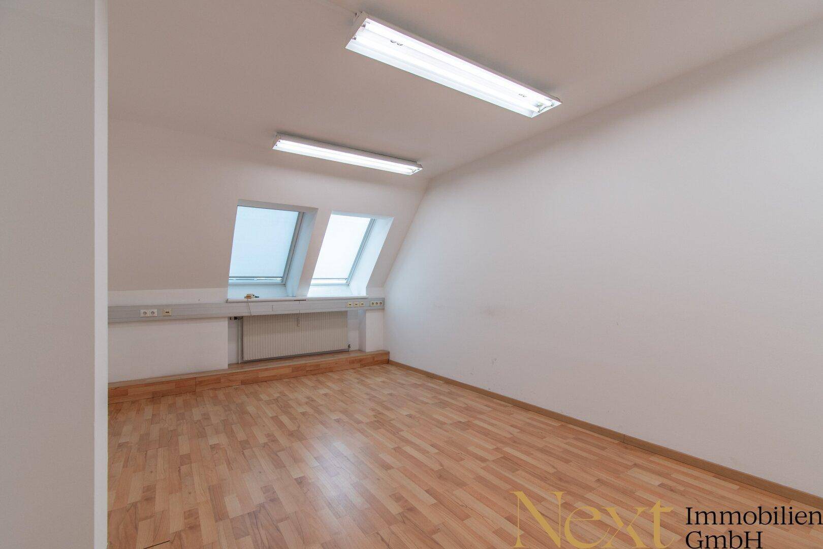 Geräumiger Büroraum im Dachgeschoss mit Laminatboden, schrägen Wänden und zwei Dachfenstern.