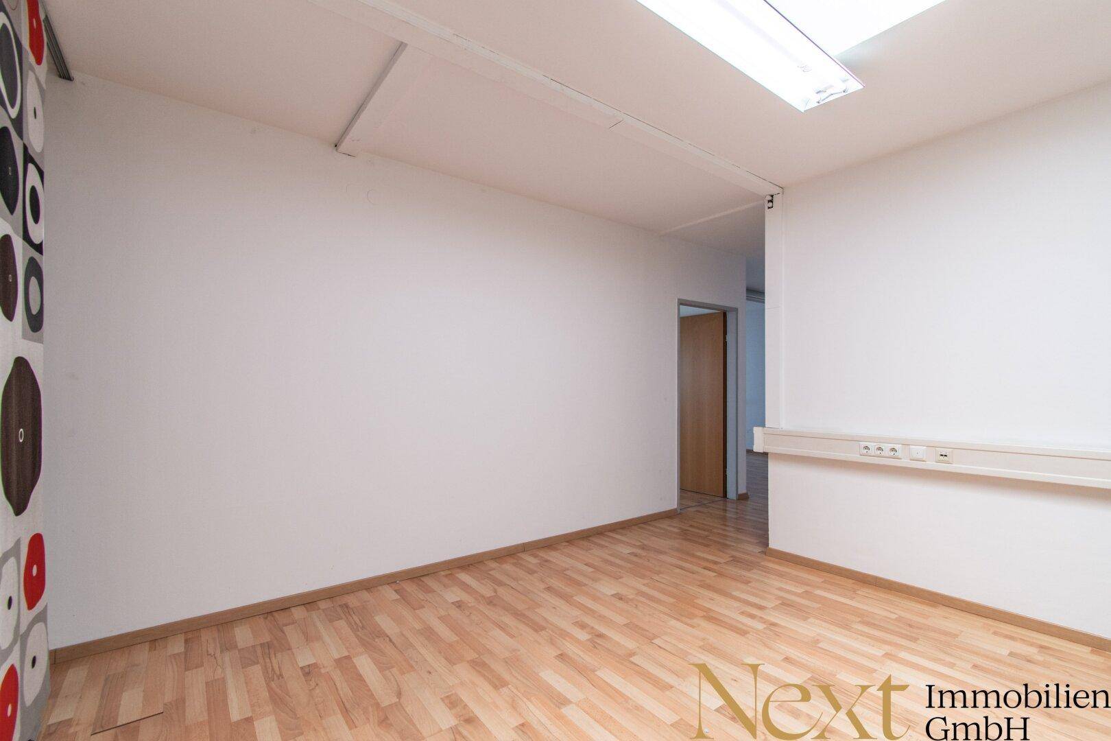 Leerer Büroraum mit hellem Laminatboden, weißen Wänden und einer dekorativen Akzentwand.