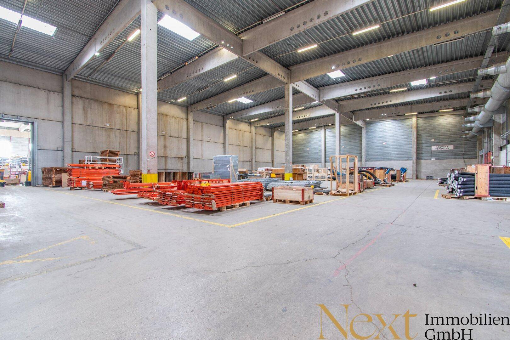 Große Lagerhalle mit hohen Decken, Betonstützen und Oberlichtern, ideal für industrielle Nutzung und Lagerung.