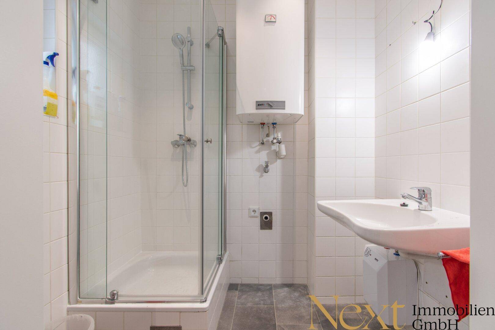 Kleines Badezimmer mit Duschkabine, Waschbecken und einem Warmwasserbereiter an der Wand.