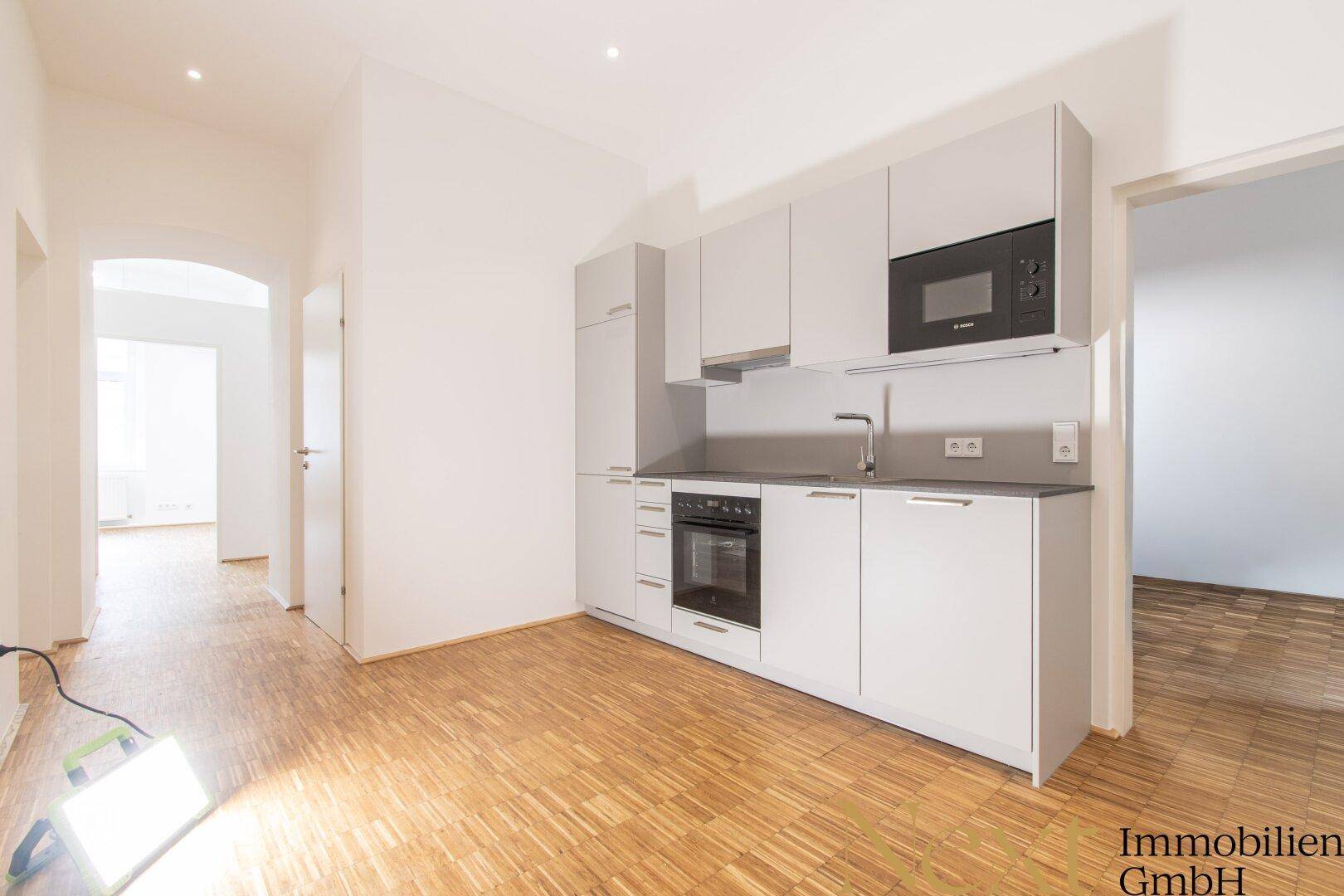 Moderne Küchenzeile mit grauen Schränken, integriertem Backofen und Mikrowelle in einem hellen Raum.