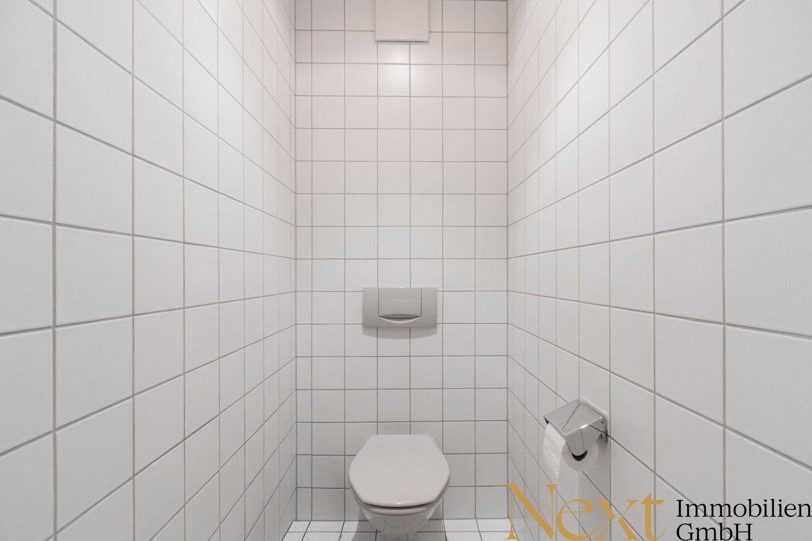 Saubere Toilette mit weißen Fliesen an Wänden und Boden, minimalistisch und funktional gestaltet.