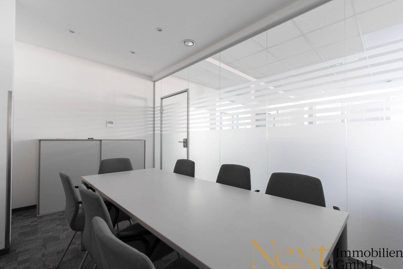 Konferenzraum mit großem Tisch und Stühlen, abgetrennt durch eine moderne Glaswand mit Sichtschutzstreifen.
