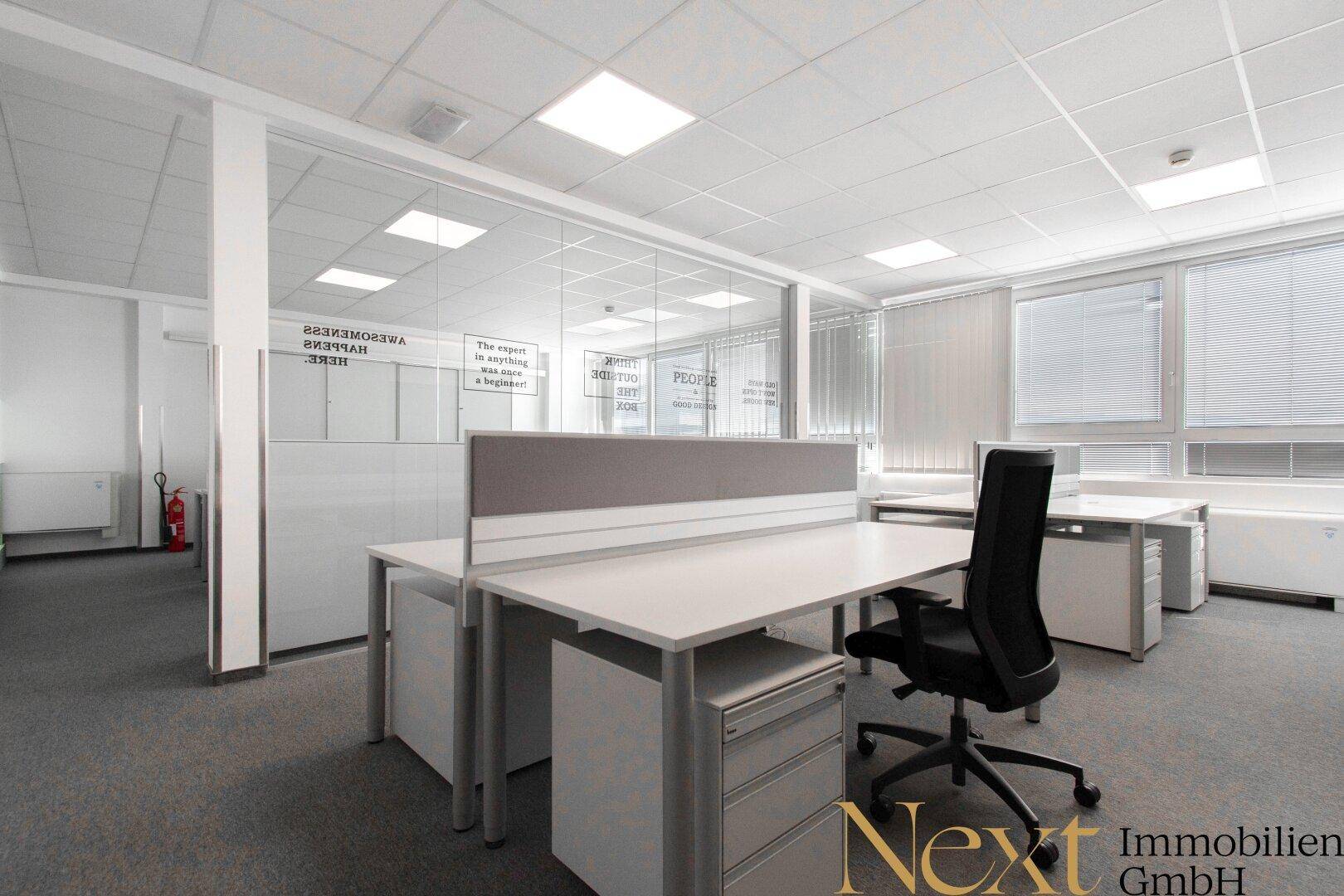Modernes Büro mit Glaswänden, die separate Bereiche schaffen, und hellen Arbeitsplätzen am Fenster.