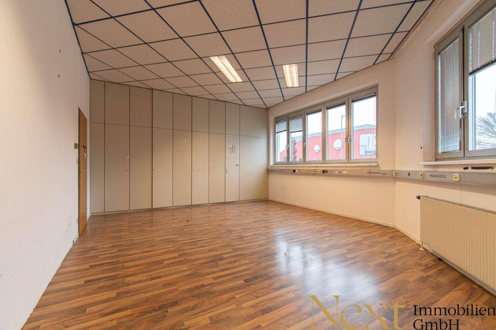 Leeres Büro mit Laminatboden, Einbauschränken und Fenstern, die viel Tageslicht hereinlassen.