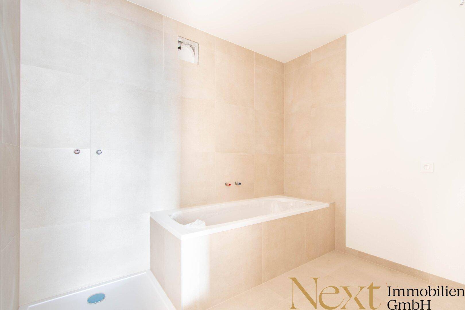Unfertiges Badezimmer mit Badewanne und Duschbereich, hell gefliest und mit Abluftventilator.