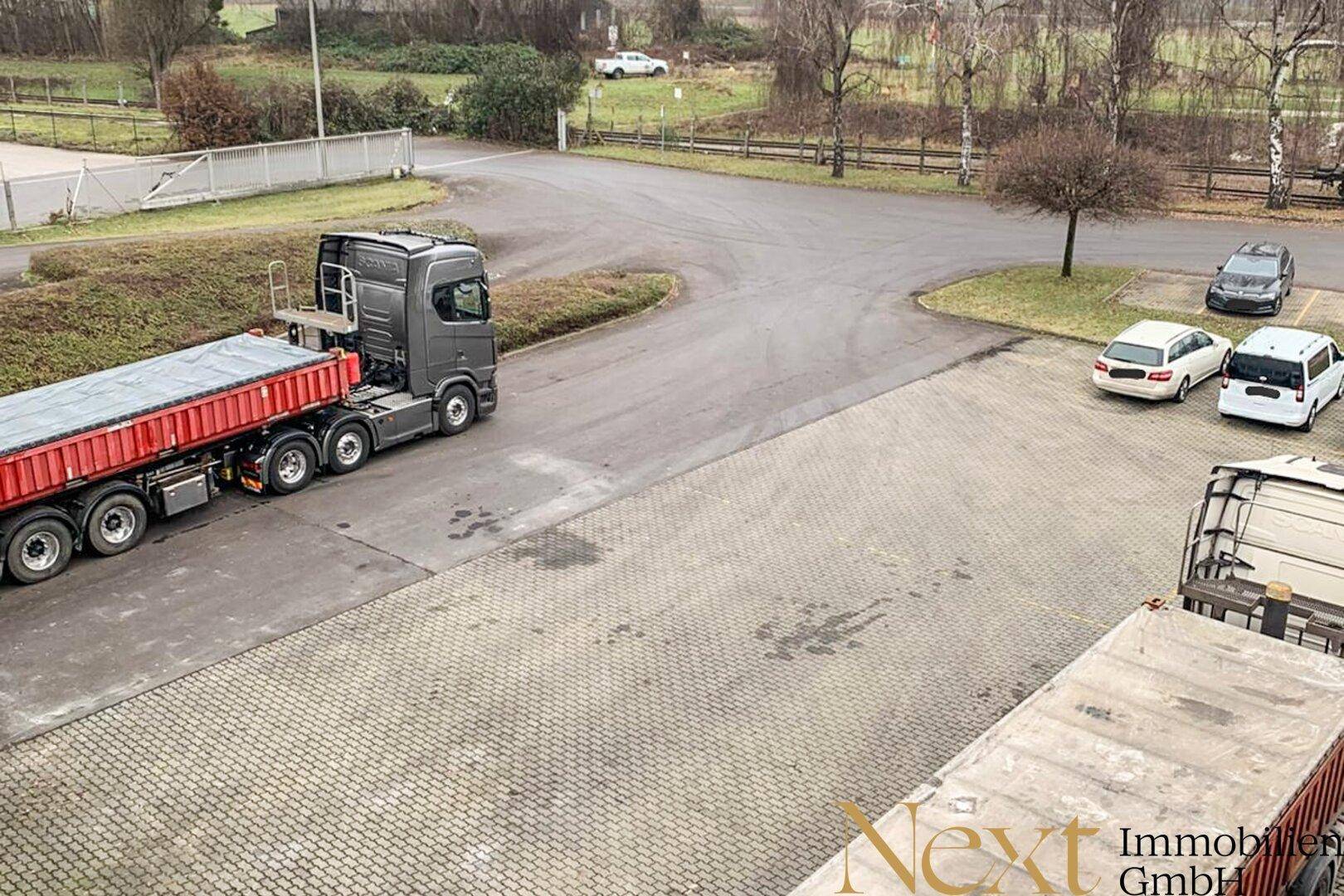 Gepflasterter Außenbereich mit Lastwagen und Zufahrt zu weiteren Gebäuden im Hintergrund des Betriebsgeländes.