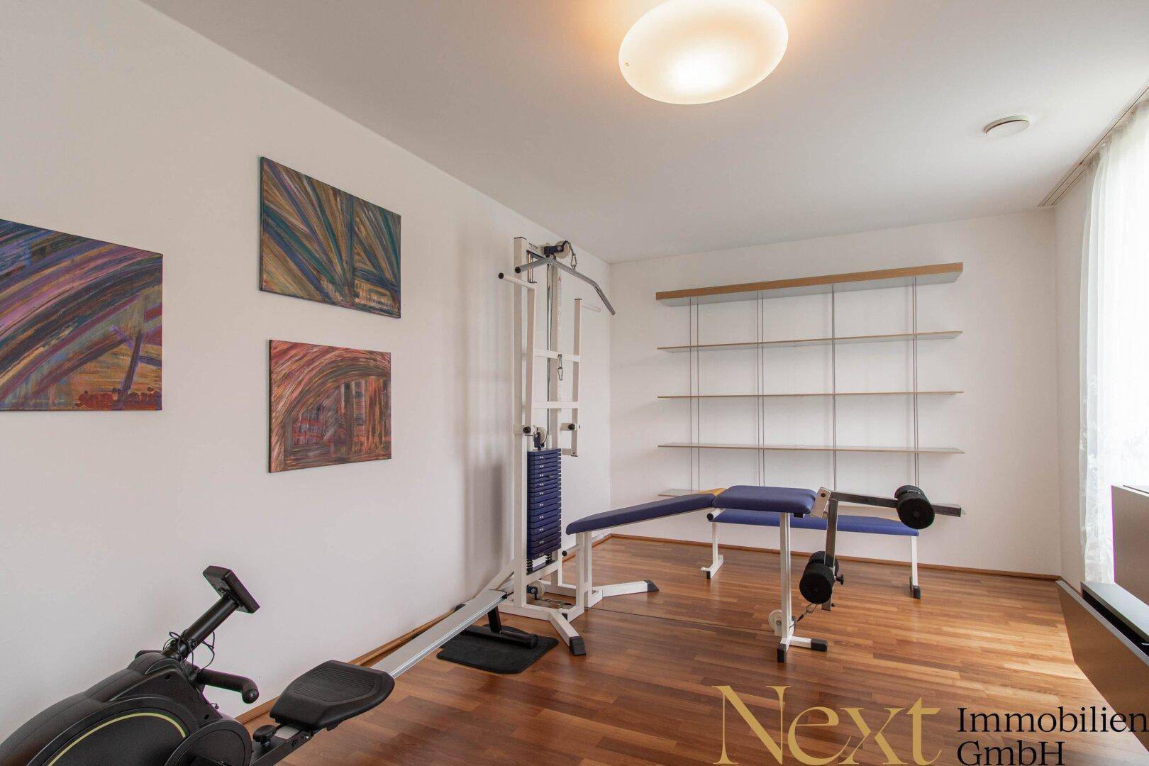 Privater Fitnessraum mit Holzboden, Trainingsgeräten und Regalen für zusätzlichen Stauraum.