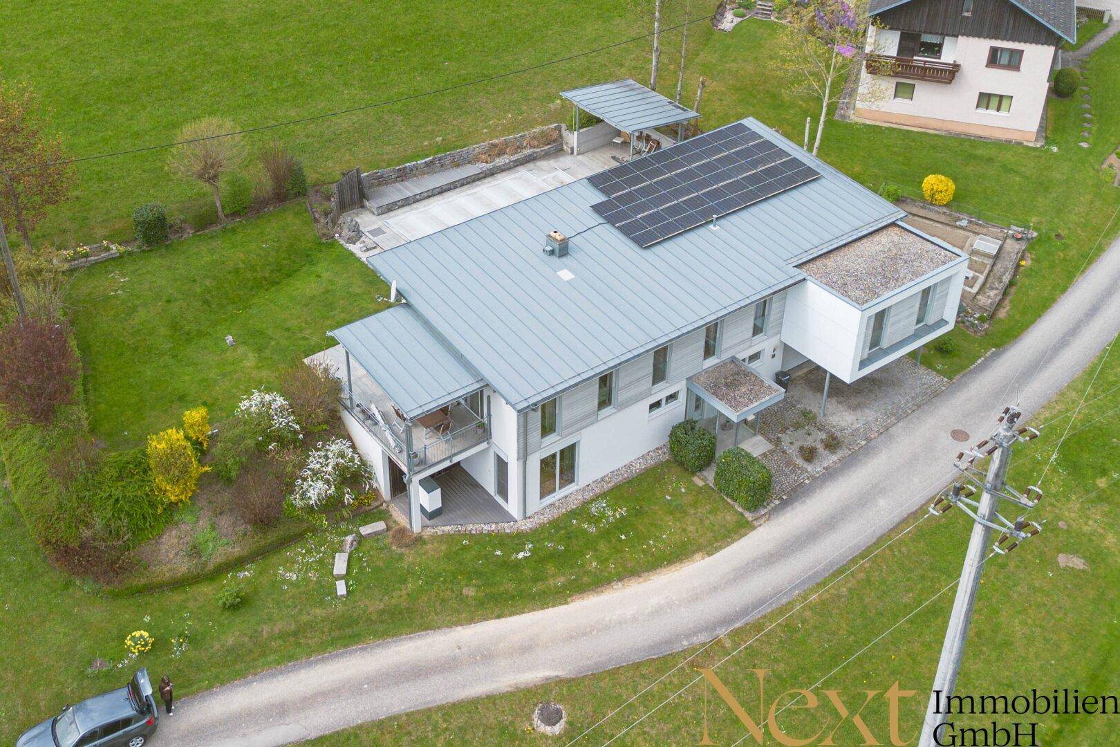Modernes Einfamilienhaus mit Photovoltaikanlage auf dem Dach, umgeben von grüner Landschaft.