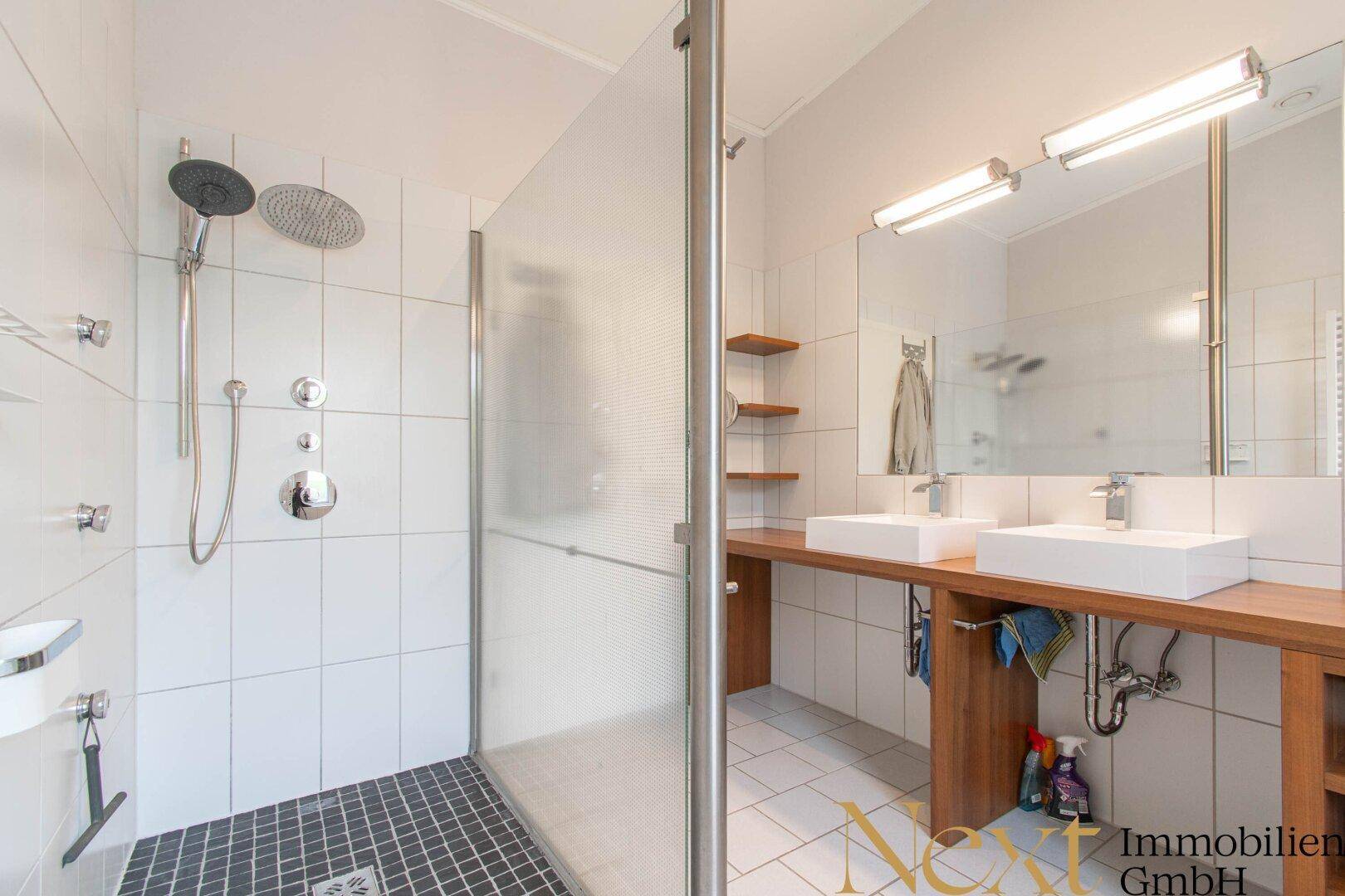 Helles Badezimmer mit großer begehbarer Dusche, Doppelwaschbecken und weißen Fliesen.