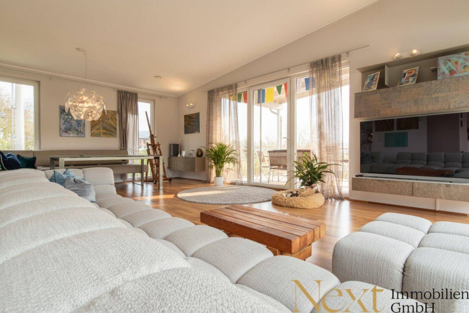 Lichtdurchfluteter Wohn- und Essbereich mit Holzboden, großem Sofa und Zugang zum Balkon.
