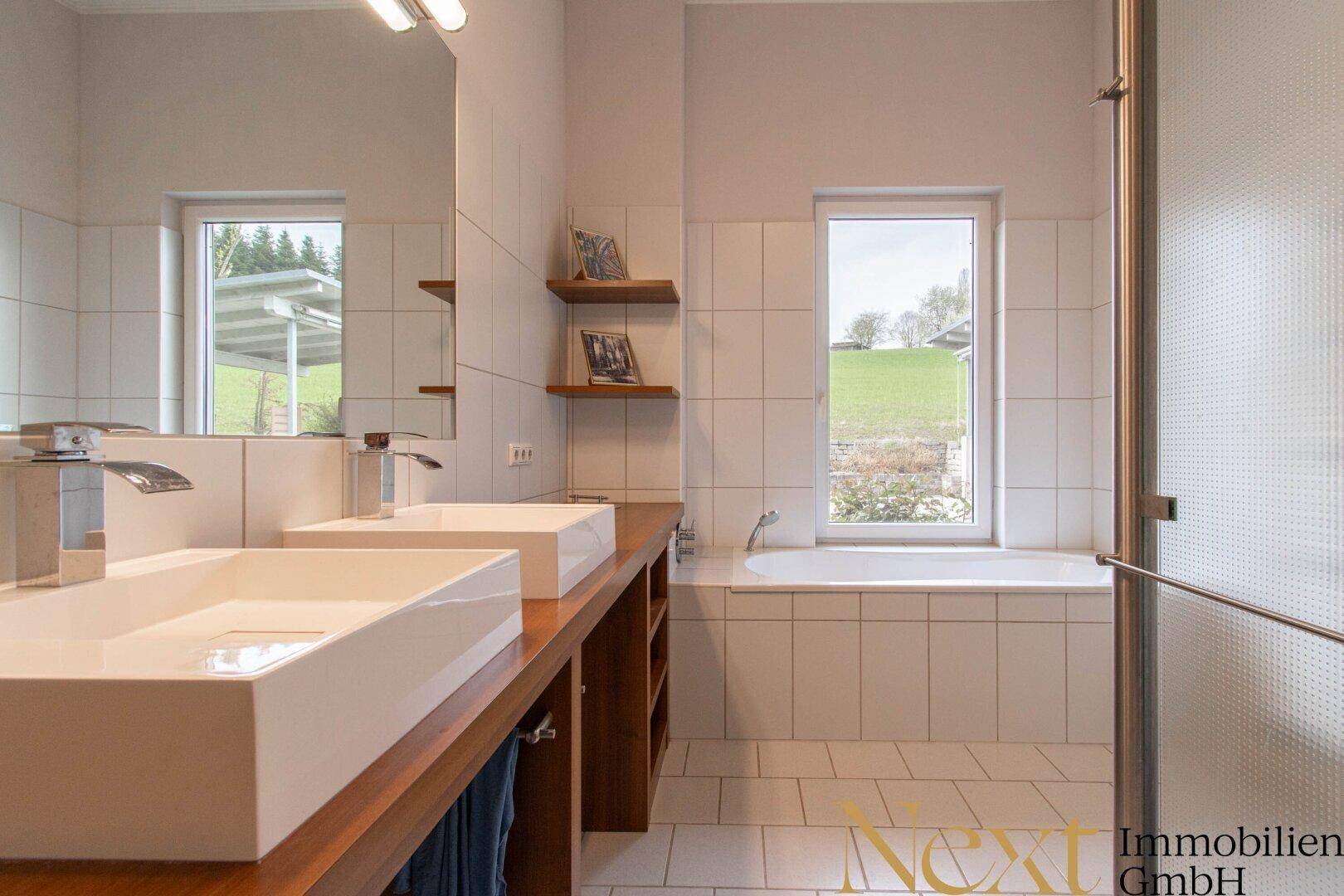 Modernes Badezimmer mit Doppelwaschbecken, Badewanne und Fenster mit Blick ins Grüne.