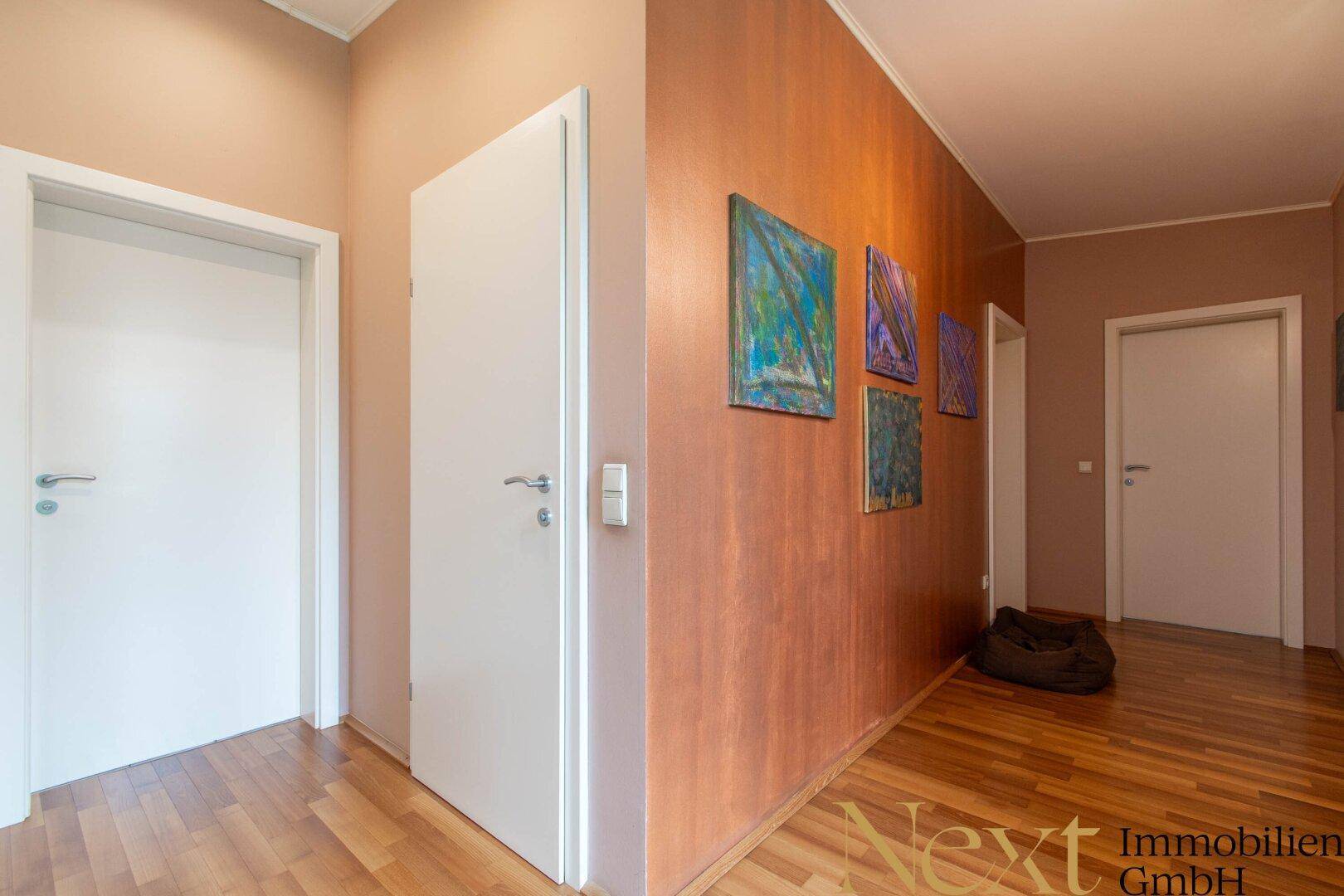 Heller Flur mit Holzboden und modernen Kunstwerken an der Wand, führt zu weiteren Räumen.