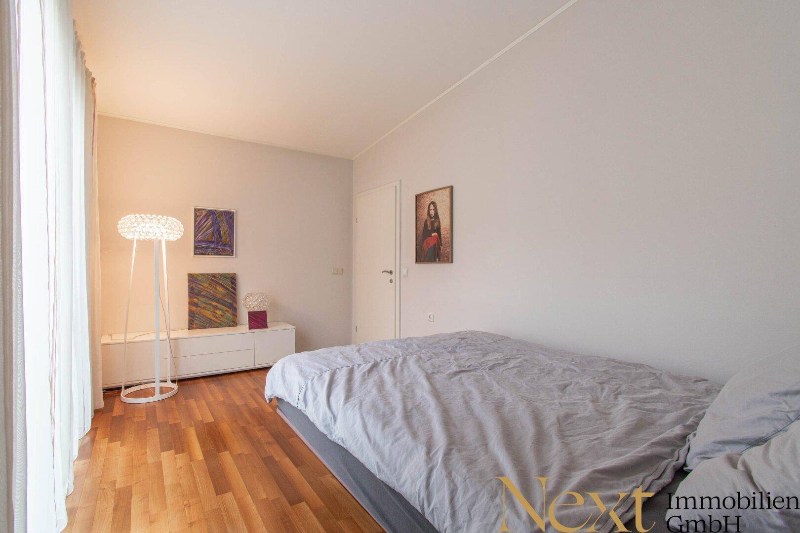 Helles Schlafzimmer mit Holzboden, modernem Bett und großem Fenster für viel Tageslicht.
