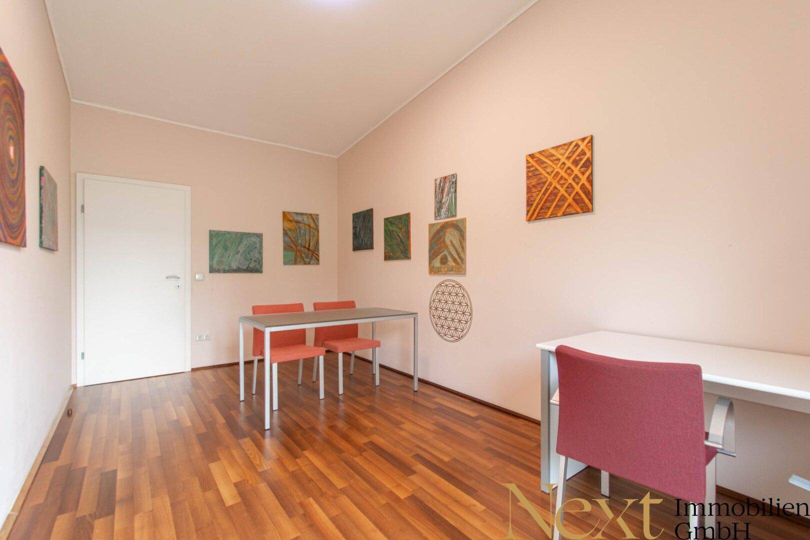 Vielseitiger Raum mit Holzboden, mehreren Tischen und farbenfrohen Kunstwerken an den Wänden.