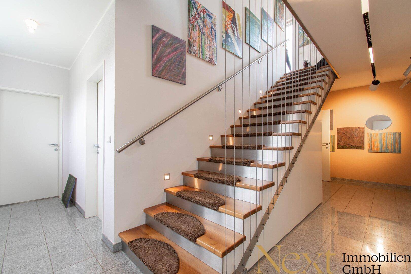 Moderne Holztreppe mit Edelstahlgeländer und integrierter Beleuchtung, führt in die obere Etage.