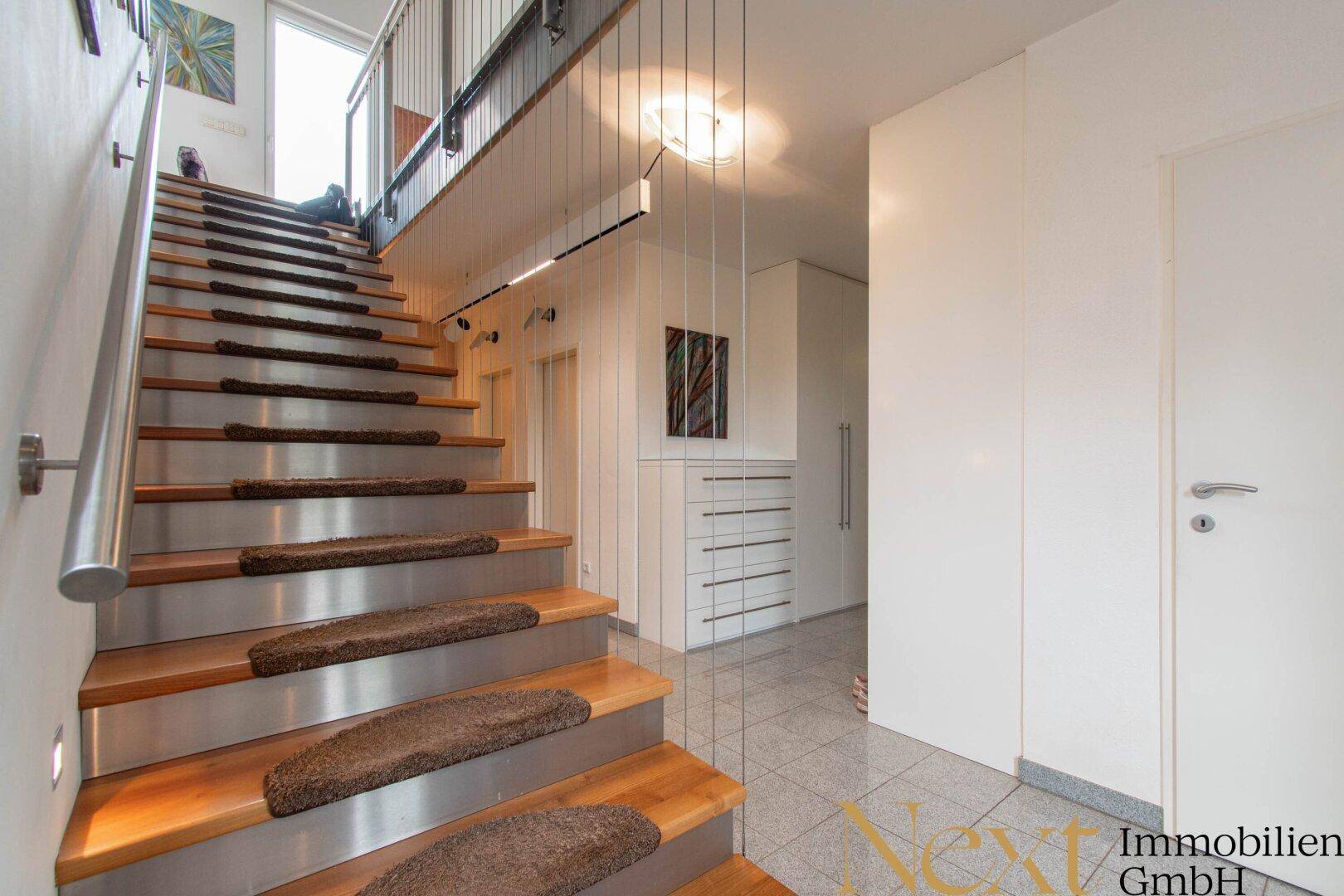 Elegante Holztreppe mit Edelstahlgeländer und Fliesenboden im Eingangsbereich des Hauses.