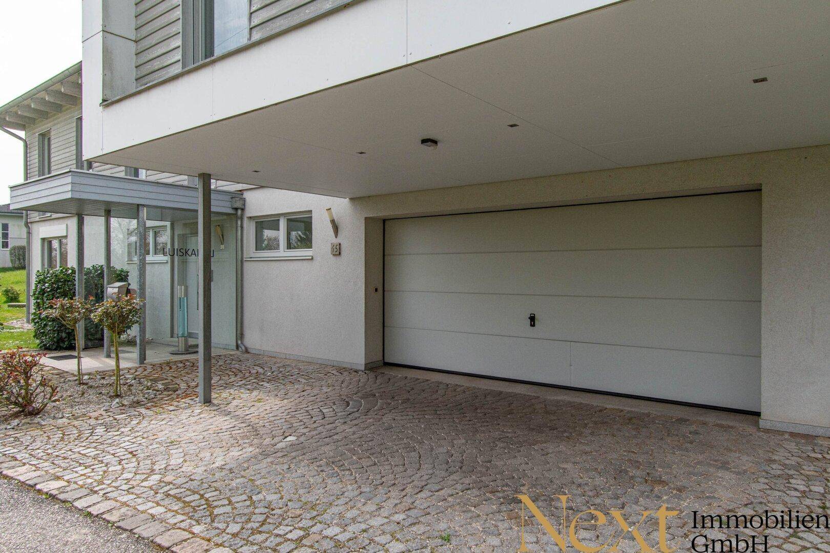 Moderne Garage mit automatischem Tor und gepflastertem Vorplatz, integriert in die Gebäudearchitektur.
