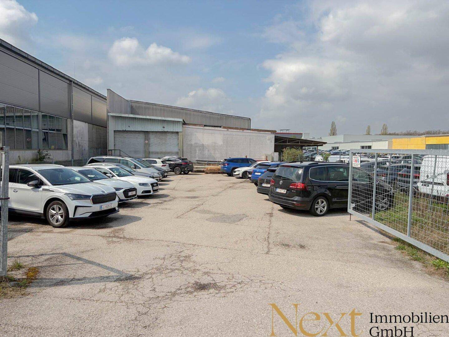 Großer Außenparkplatz mit zahlreichen Fahrzeugen und einem Industriegebäude im Hintergrund.