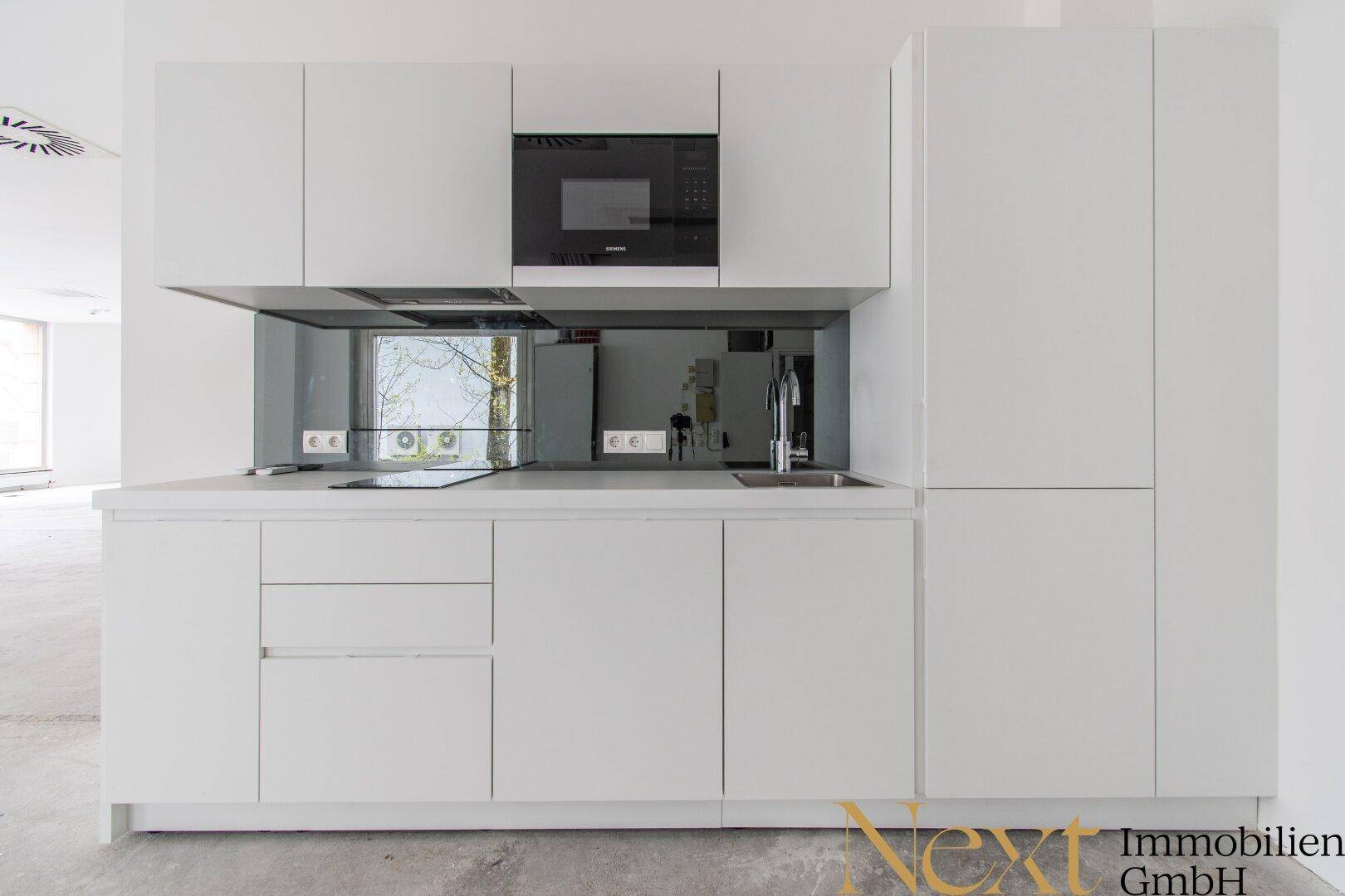 Moderne, weiße Küchenzeile mit integrierter Mikrowelle, Spüle und Induktionskochfeld.