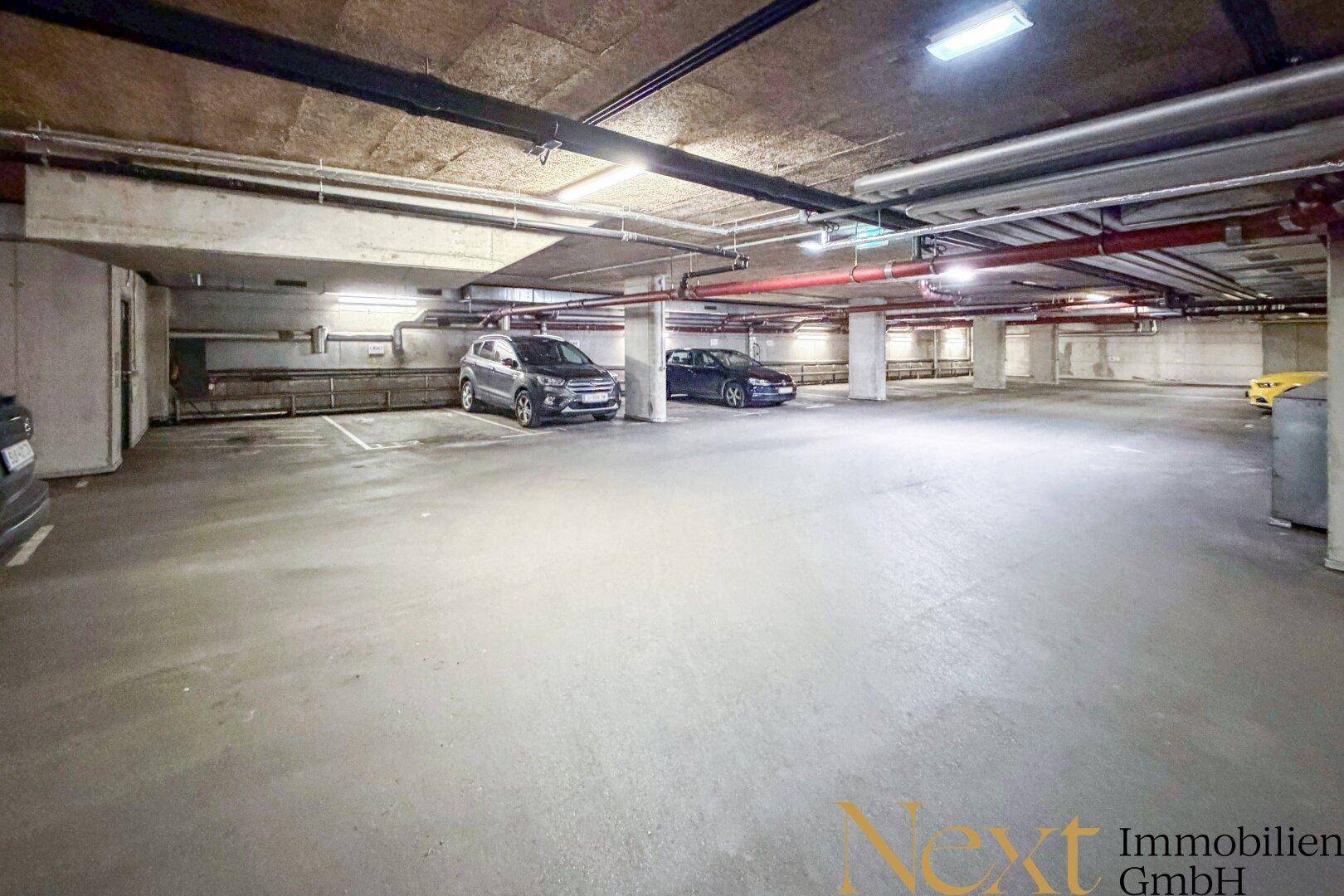 Geräumige Tiefgarage mit mehreren Stellplätzen und sichtbaren Versorgungsleitungen an der Decke.
