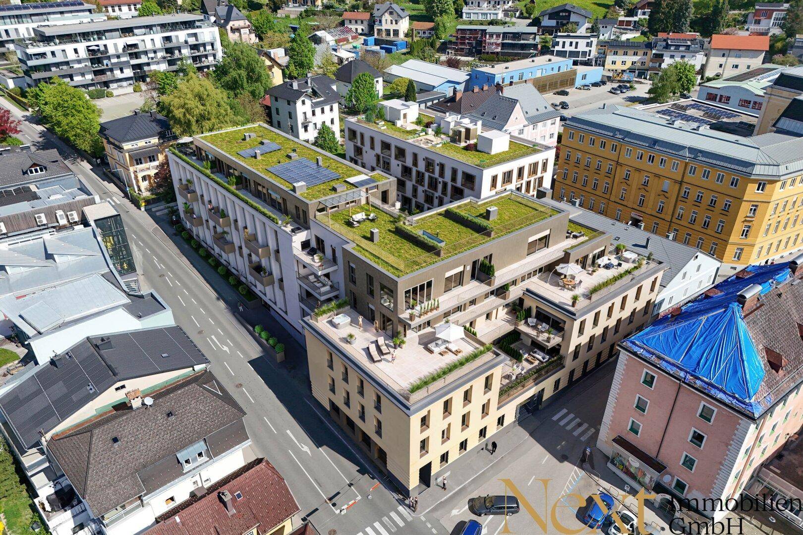 Luftaufnahme eines modernen Wohnkomplexes mit begrünten Flachdächern, Balkonen und Dachterrassen in städtischer Umgebung.
