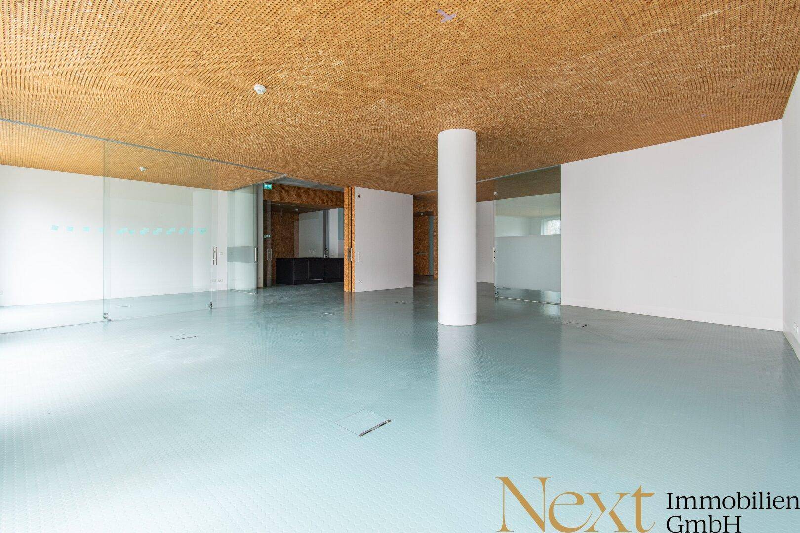 Moderner Büroraum mit flexiblen Glaswänden und einer Säule, ideal für verschiedene Arbeitsbereiche.