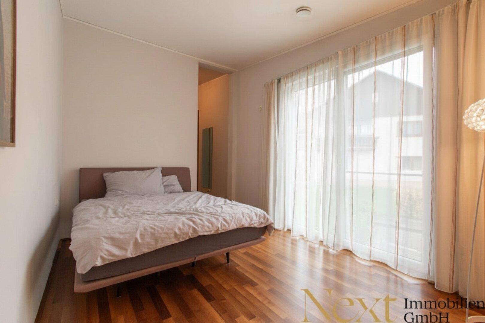 Schlafzimmer mit Holzboden, großem Fenster und Zugang zu einem Balkon oder Terrasse.