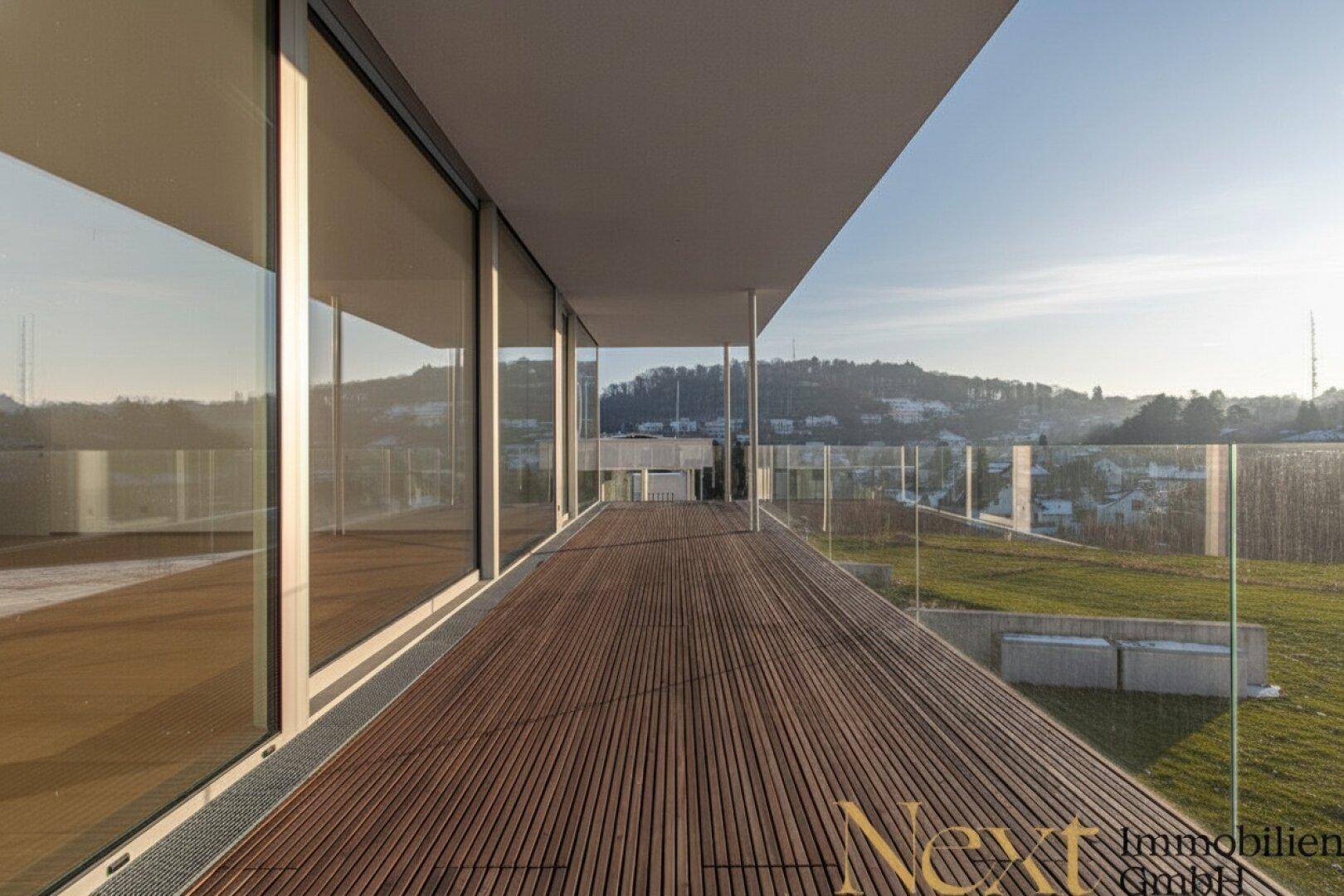 Geräumiger Balkon mit Holzdeck, raumhohen Fenstern und Panoramablick auf die grüne Umgebung.