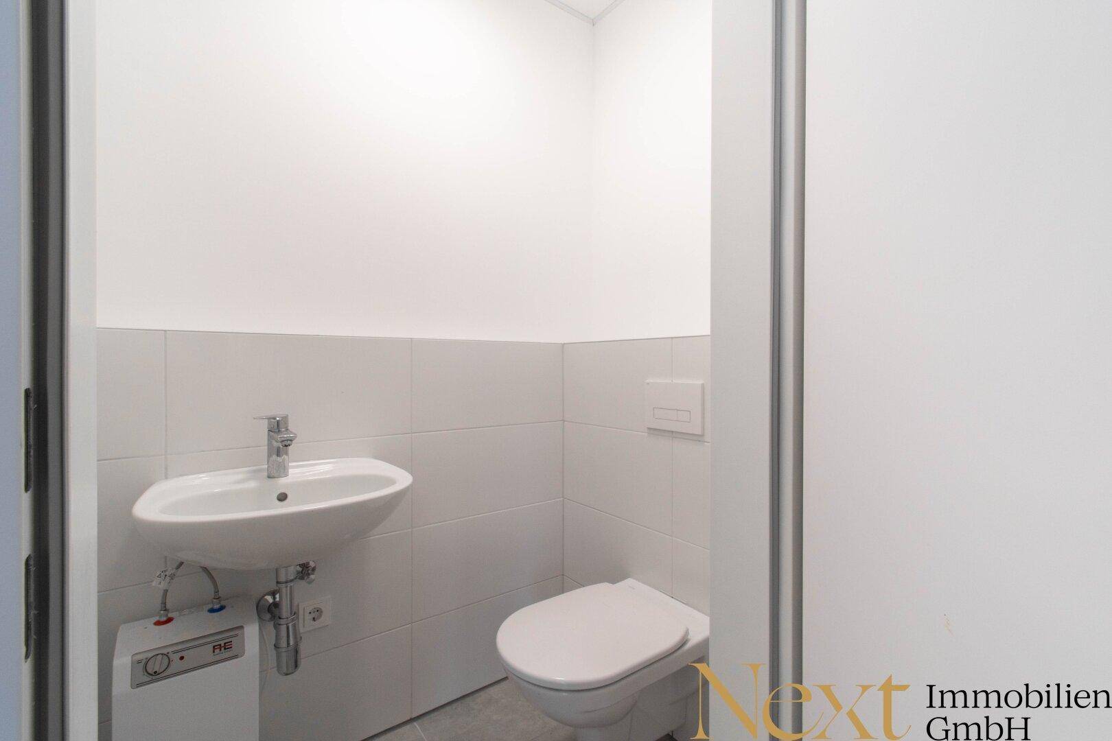 Kleines, helles Gäste-WC mit weißen Fliesen, Waschbecken und Wand-WC.