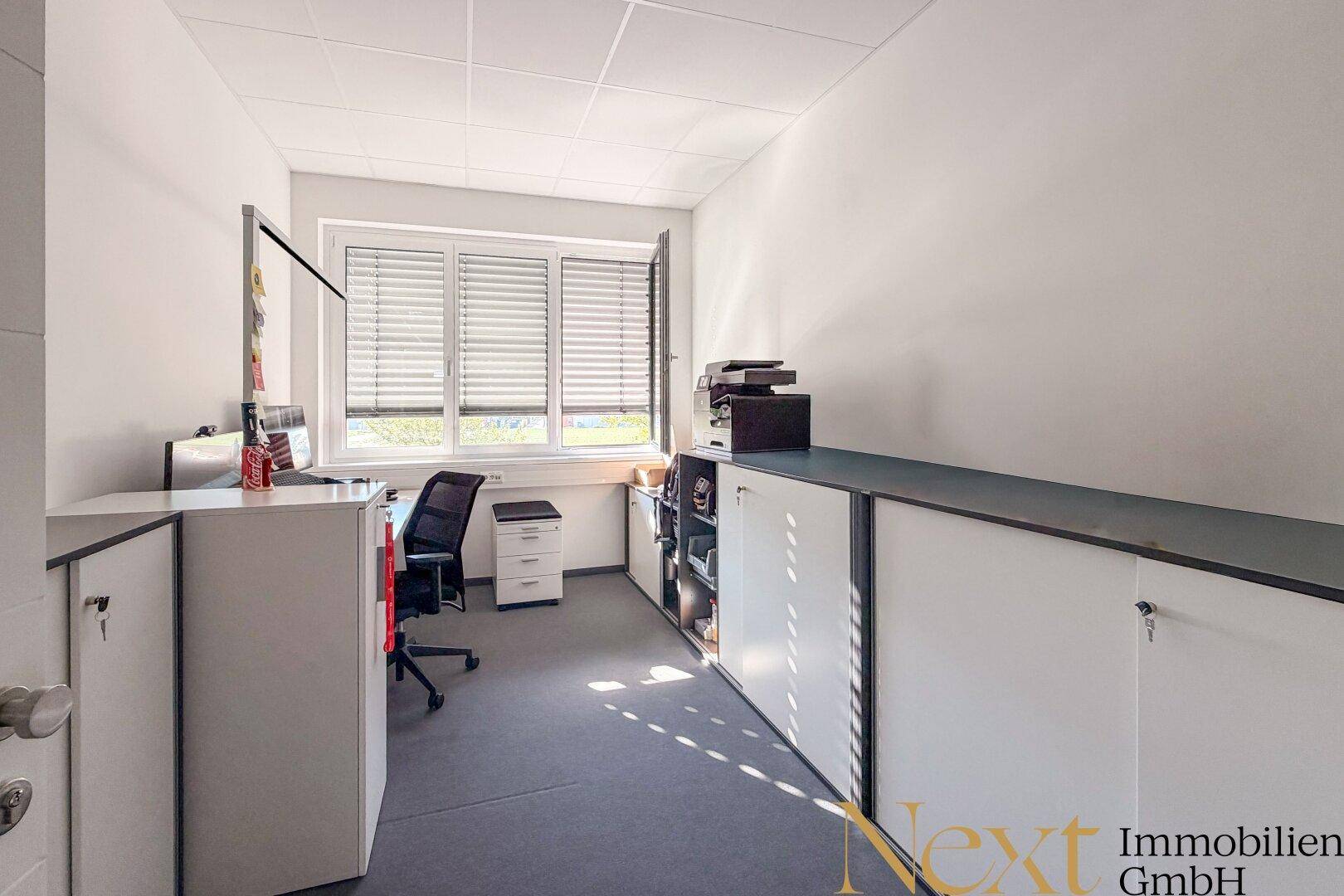 Kleineres Büro oder Archivraum mit Schreibtisch, Drucker und praktischen Einbauschränken unter dem Fenster.