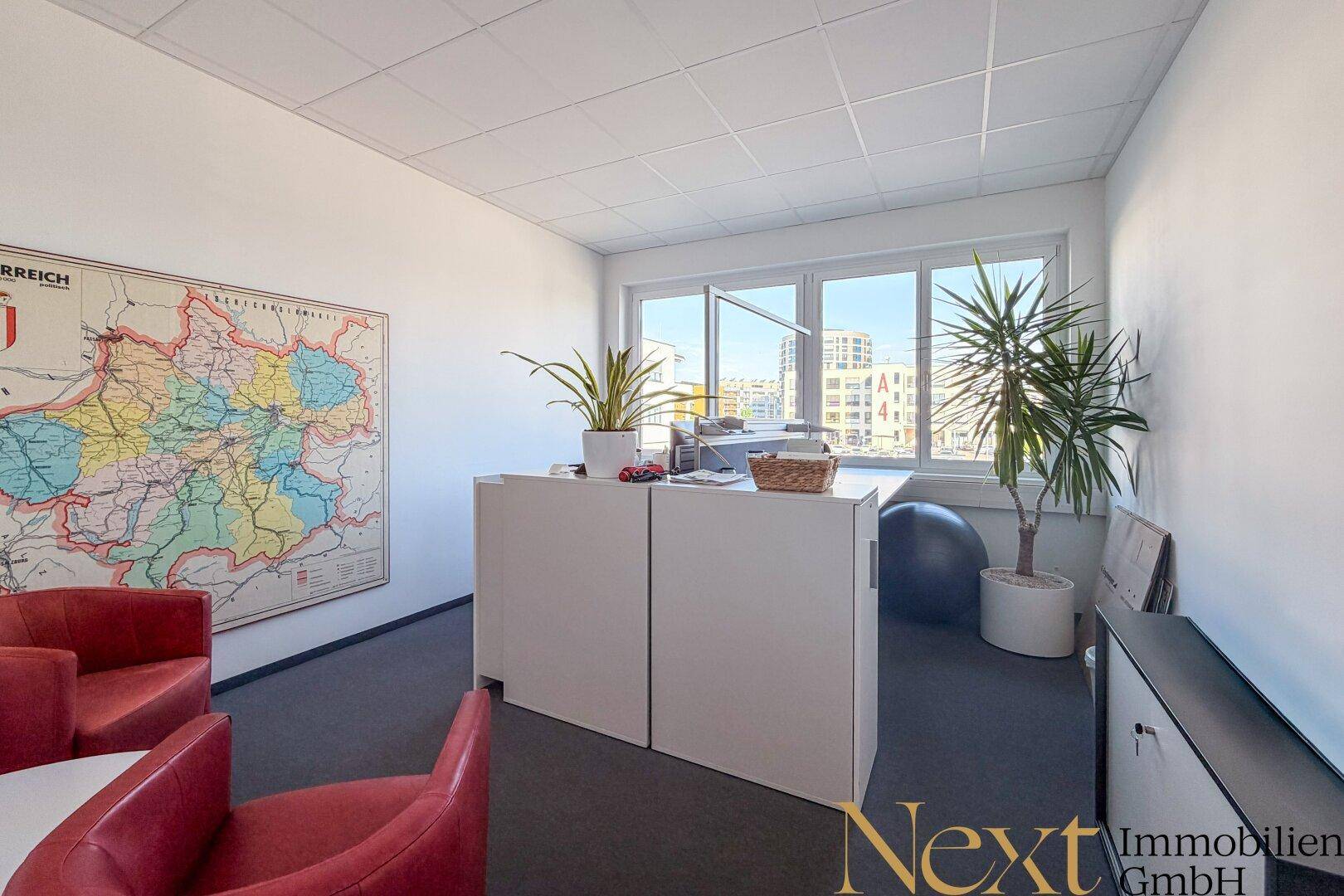 Büro mit großen Fenstern, einem Kartenausschnitt an der Wand und roten Sesseln.