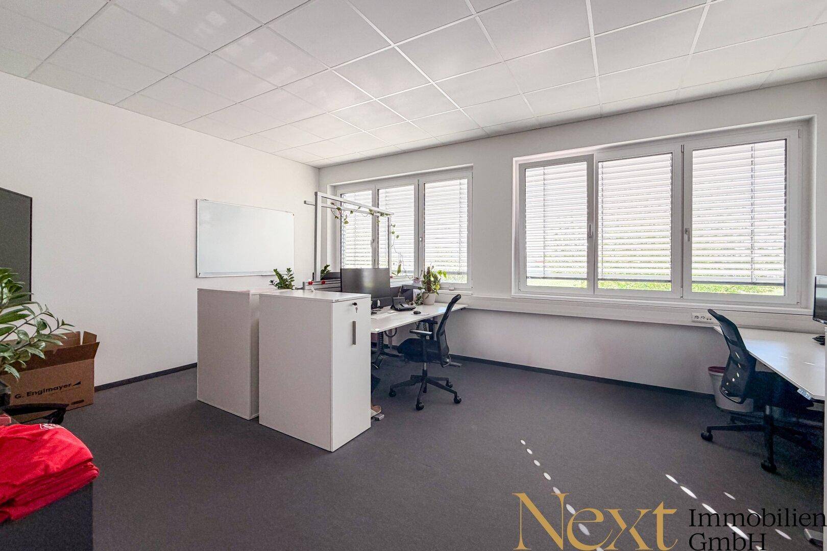 Geräumiges Büro mit mehreren Arbeitsplätzen, großen Fenstern und Jalousien.