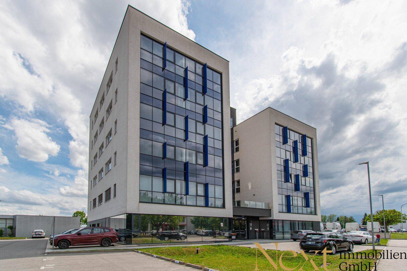 Modernes Bürogebäude mit markanter Glasfassade und blauen Akzenten unter bewölktem Himmel.