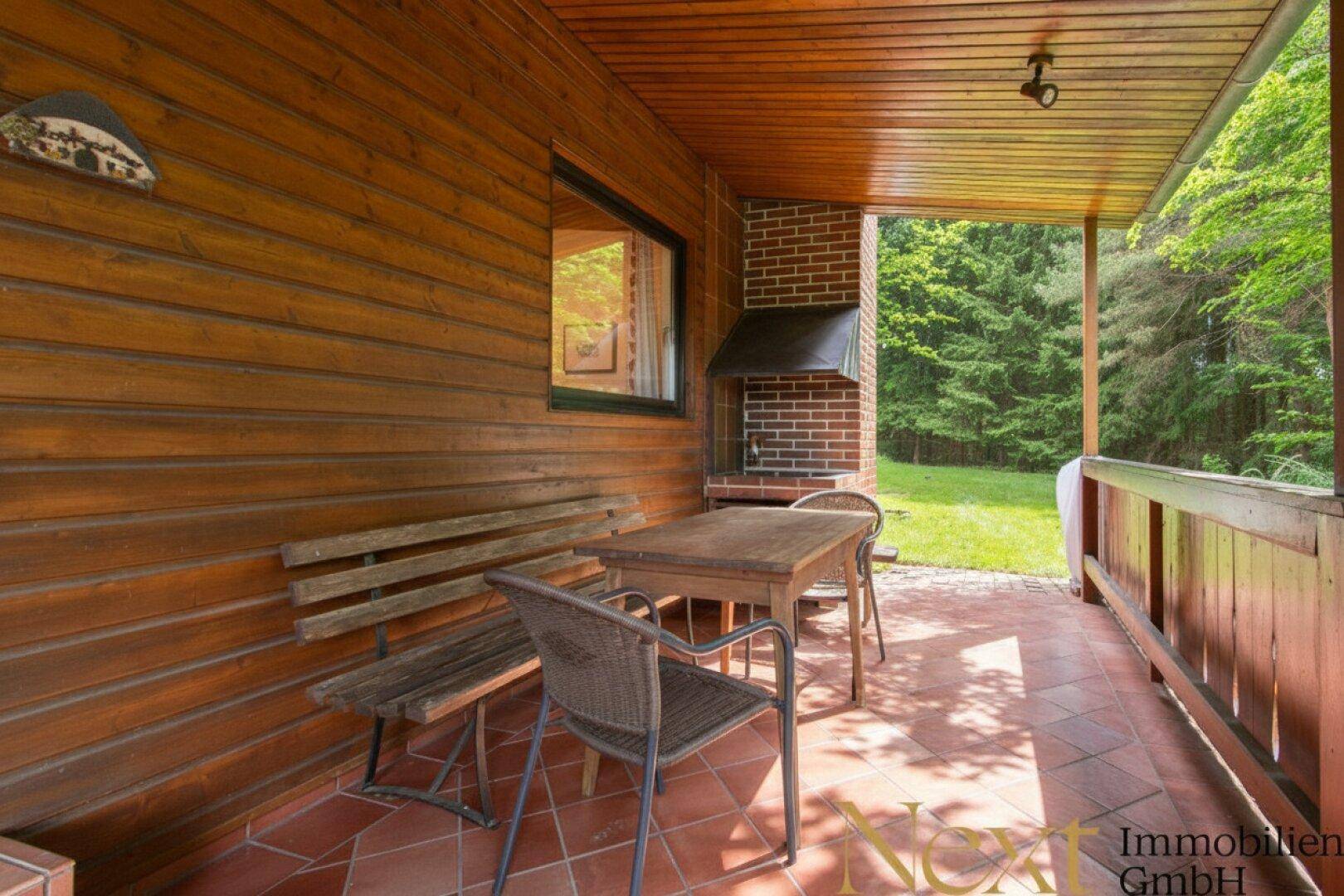 Überdachte Terrasse mit Holzwänden, Fliesenboden und einem gemauerten Grill, ideal für gesellige Abende.