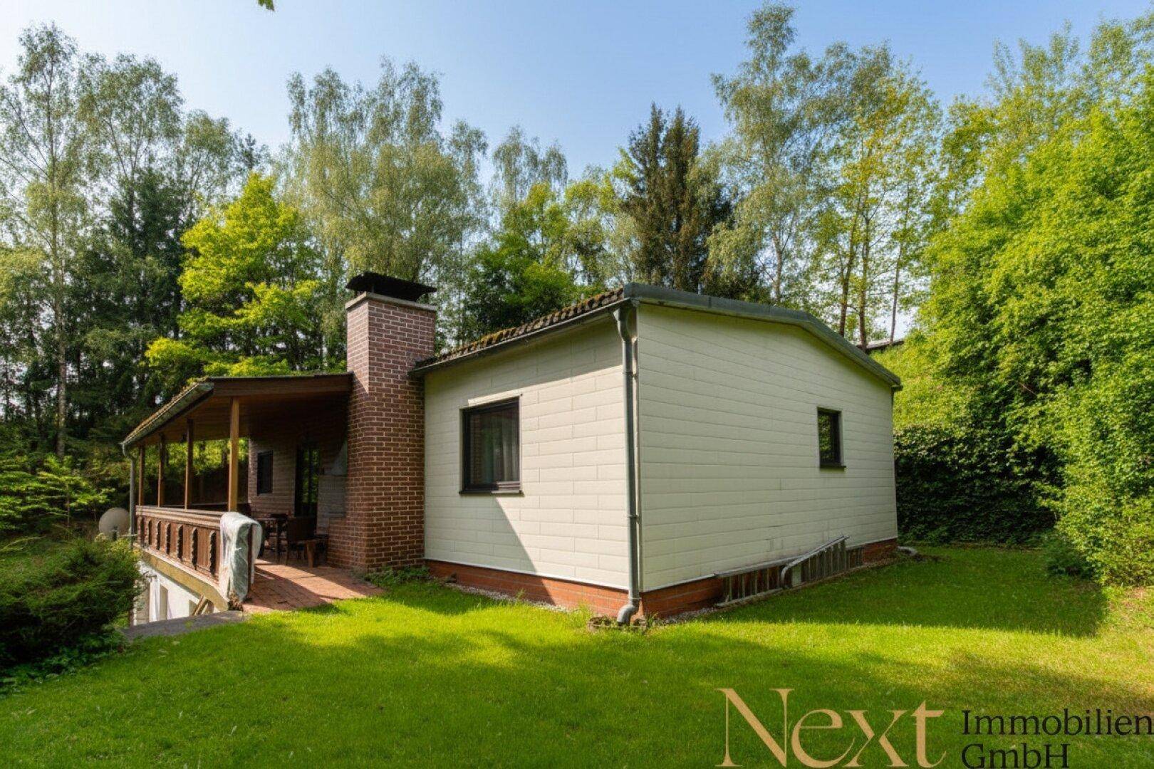 Rückansicht des Hauses mit einem markanten Kamin und einem weitläufigen Gartenbereich, umgeben von Natur.