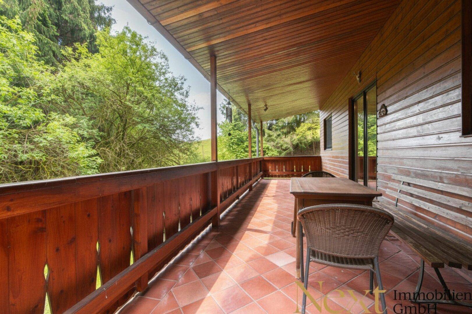 Lange überdachte Terrasse mit Holzbalkon und einem weiten Blick in die grüne, hügelige Landschaft.