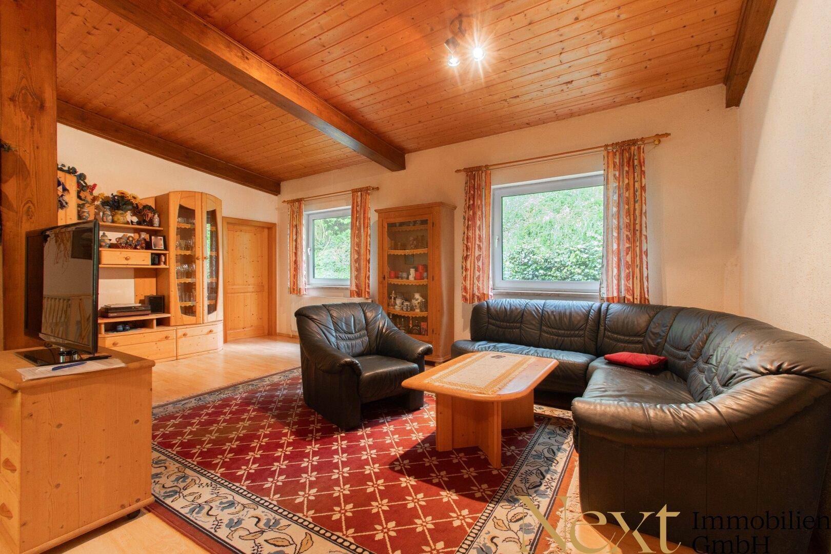 Wohnzimmer mit bequemen Ledersofas, Holzbalkendecke und einem Teppich, der eine warme Atmosphäre schafft.