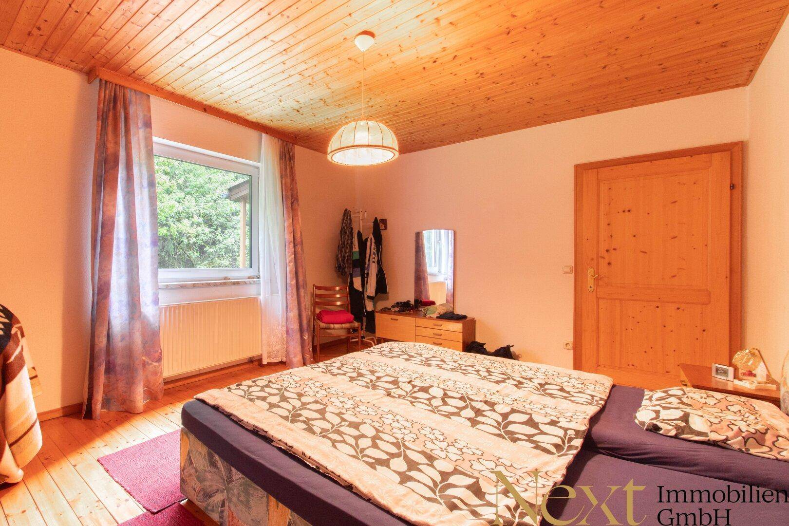Gemütliches Schlafzimmer mit Doppelbett, Holzbalkendecke und einem Fenster mit Blick in die Natur.