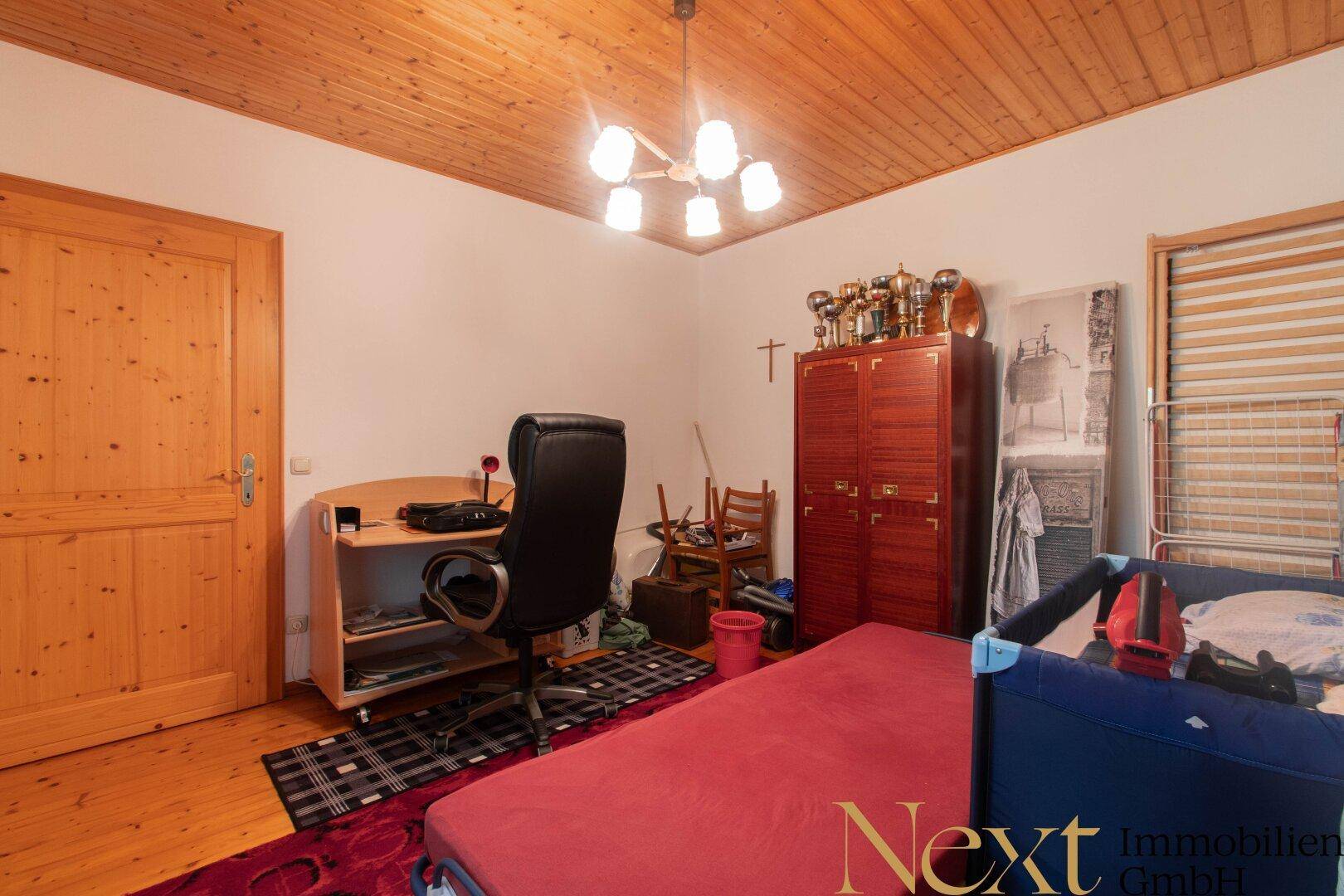Vielseitiges Zimmer, nutzbar als Kinder- oder Gästezimmer, mit Bett, Schreibtisch und Holzmöbeln.