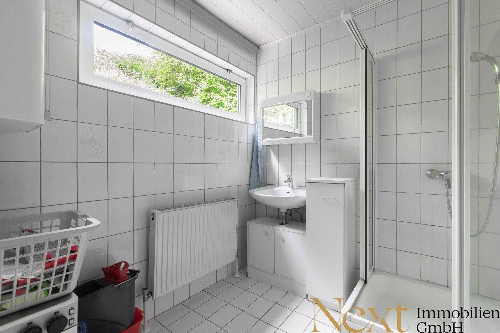 Helles Badezimmer mit Dusche, Waschbecken und einem Fenster, komplett mit weißen Fliesen ausgestattet.