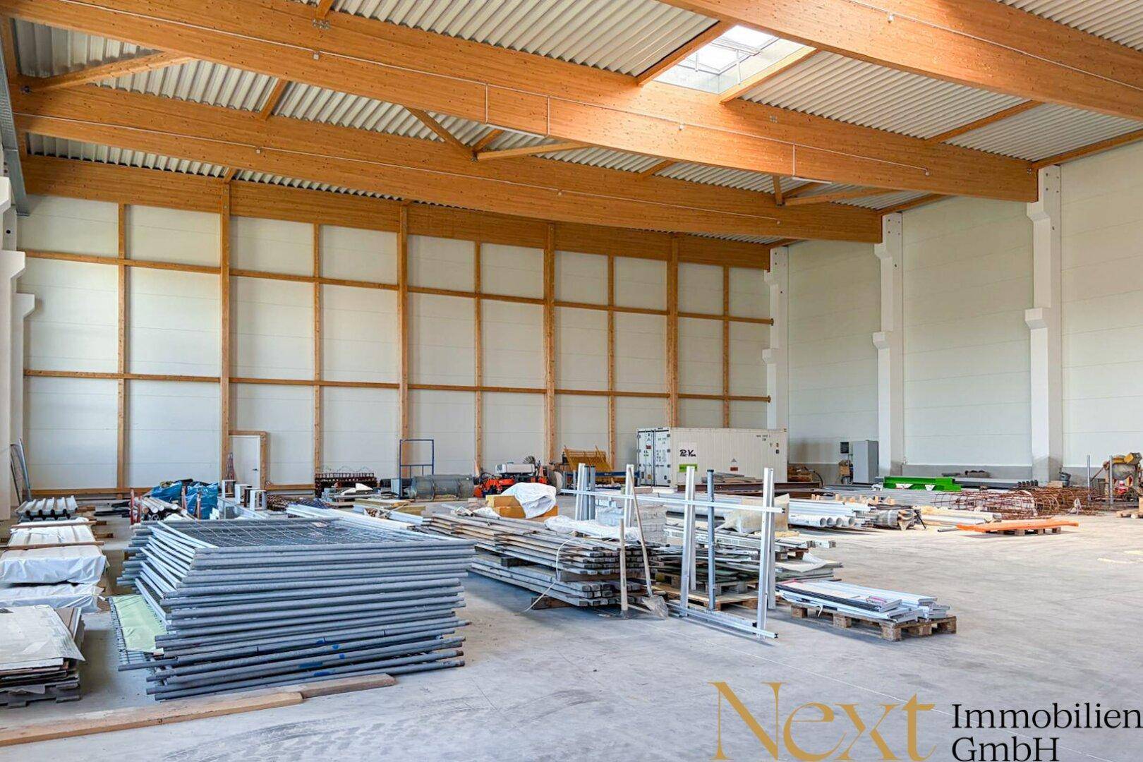 Große Industriehalle mit hohen Decken, Holzbalken und Betonboden, derzeit im Bau mit Materialien.