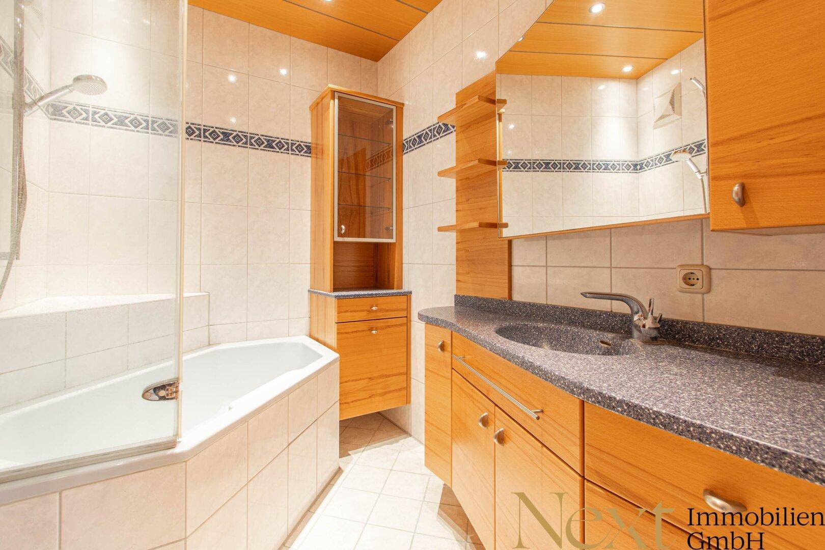 Gefliestes Badezimmer mit Badewanne, Dusche und Holzmöbeln.