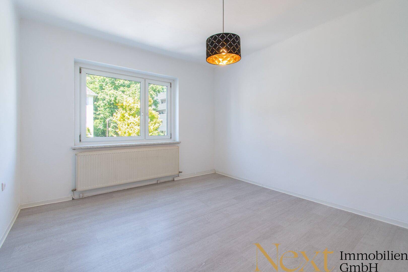 Helles Schlafzimmer mit modernem Laminatboden, weißen Wänden und einem Fenster mit Blick ins Grüne.