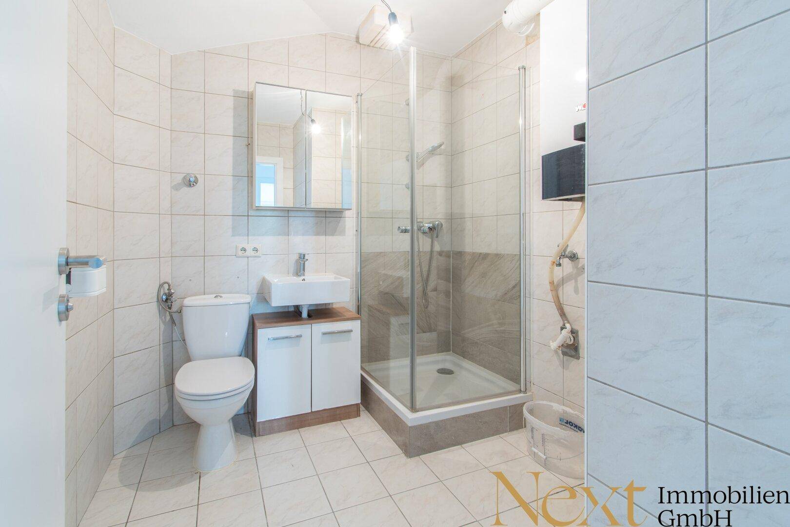 Funktionales Badezimmer mit hellen Fliesen, Duschkabine, WC und einem Waschbecken mit Spiegelschrank.