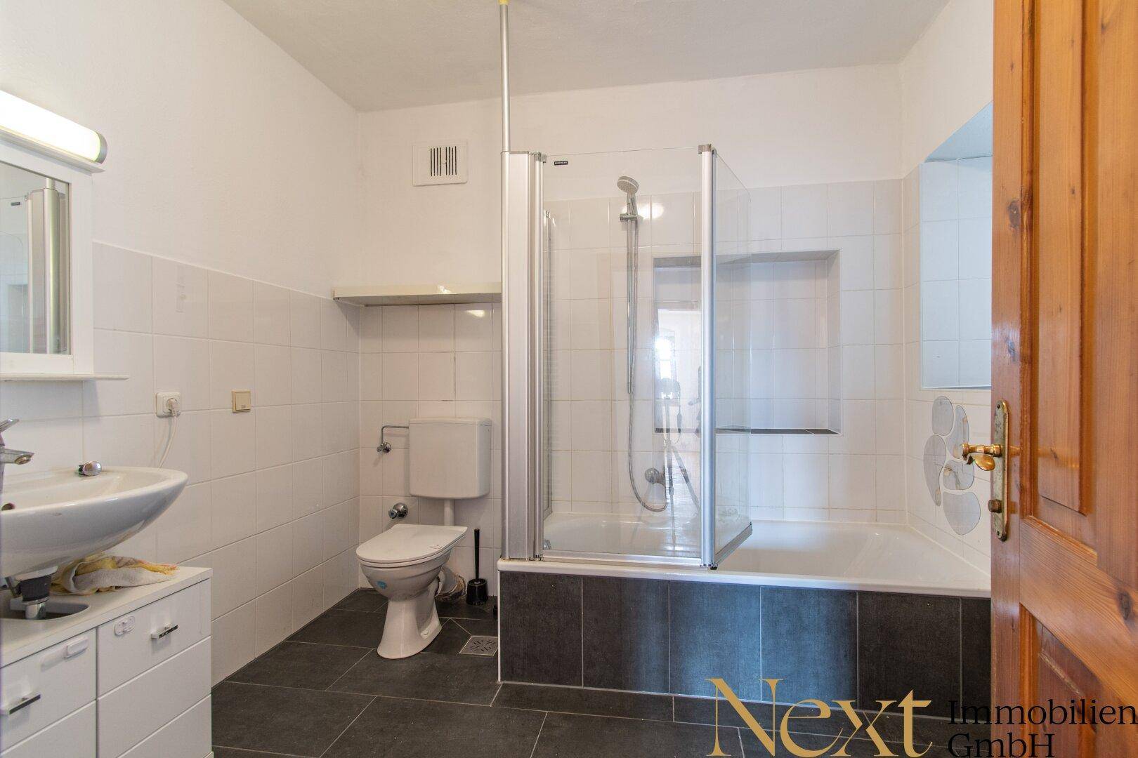 Modernisiertes Badezimmer mit Badewanne und Duschabtrennung, Waschbecken und WC.