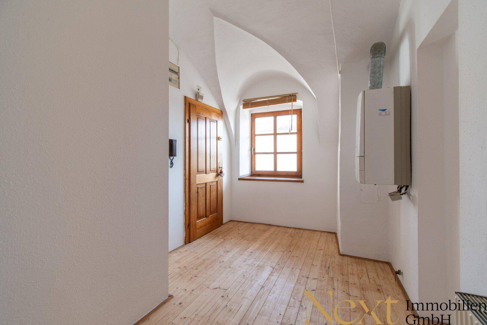 Kleiner Raum mit Holzdielenboden, Gewölbedecke und einem Fenster, das Tageslicht hereinlässt.