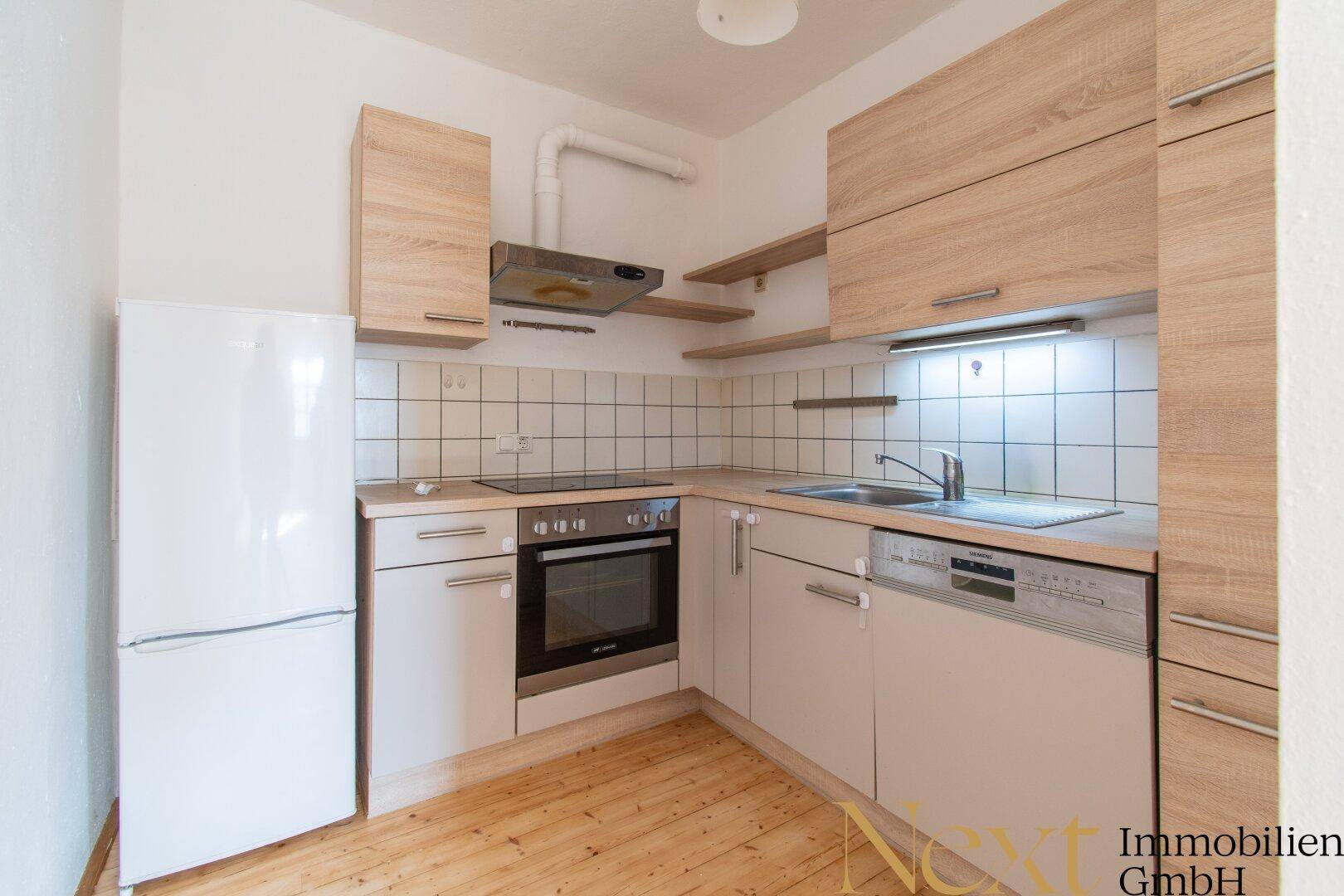 Funktionale Einbauküche mit hellen Holzfronten, Fliesenrückwand und modernen Geräten.