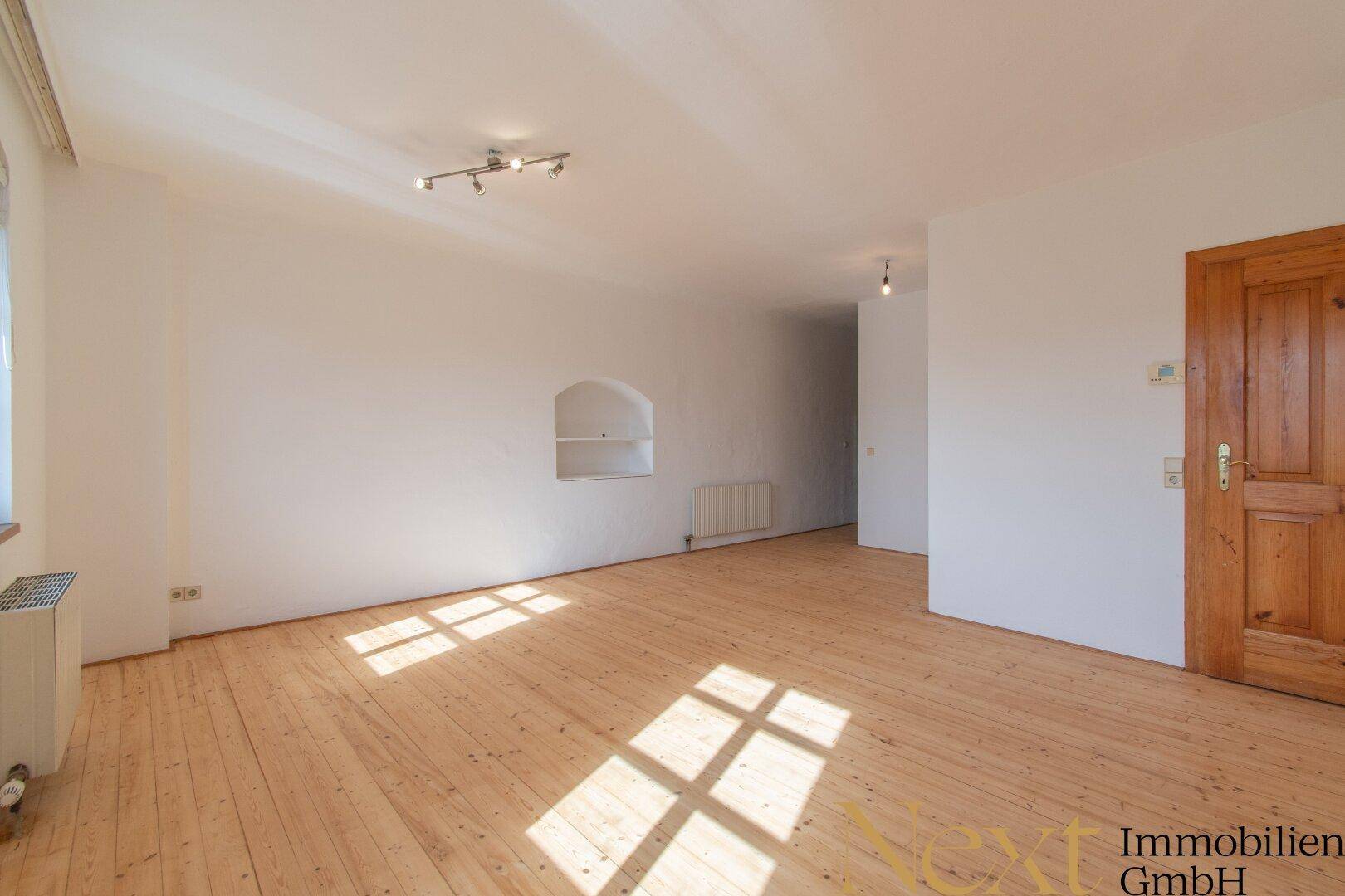 Geräumiges Wohnzimmer mit Holzdielenboden, weiß gestrichenen Wänden und natürlichem Lichteinfall.